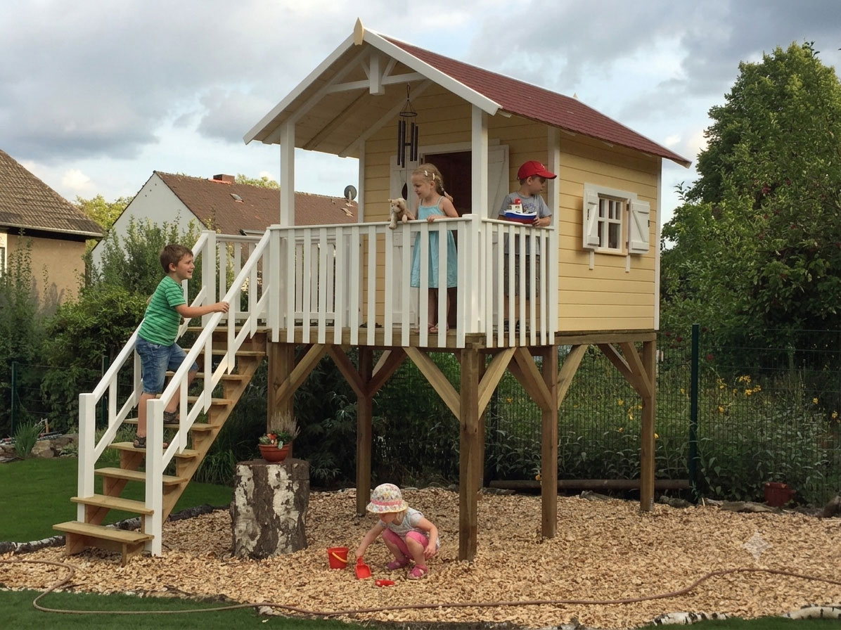Spielende Kinder am gelben Stelzenhaus Janson XXL-A5 Spielhaus im Garten